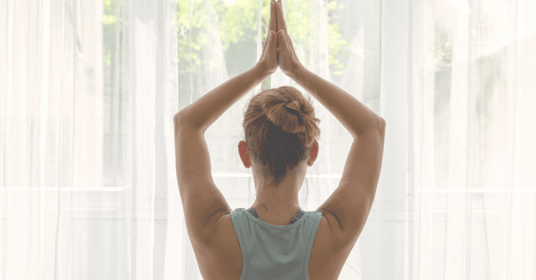 woman facing the window hands over head with palms together at the beginning of Sun Salutaiton sequence